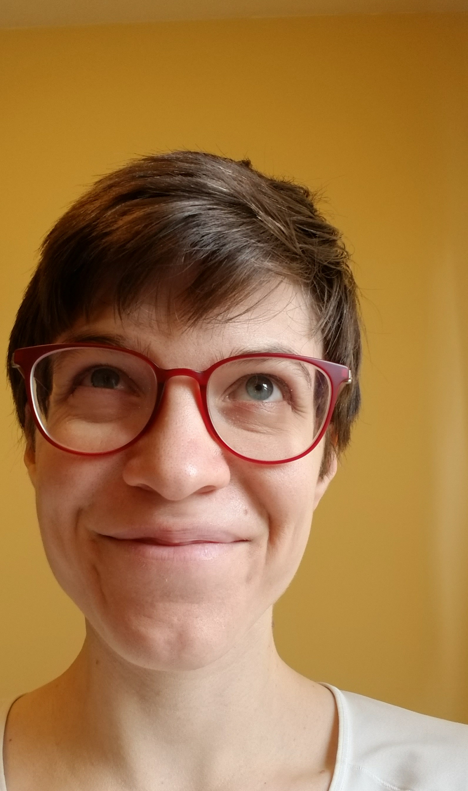 Emily smiling and looking up, wearing red glasses against a yellow background